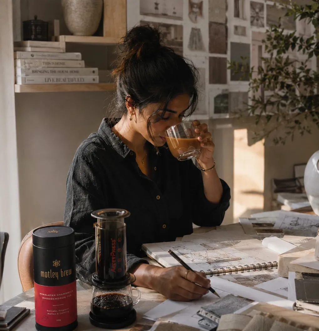 A designer sips tea at her desk beside a Motley Brew tin